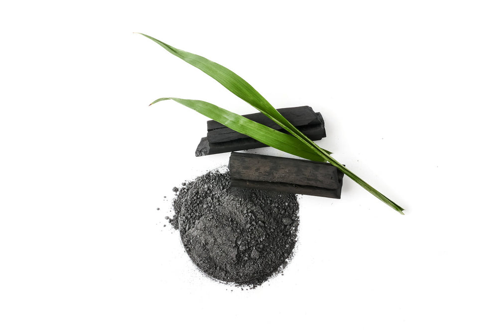 Carvão ativado: saiba o que é, pra que serve, benefícios e como usar Pilha de carvão vegetal, pó de carvão e folhas verdes ao redor.