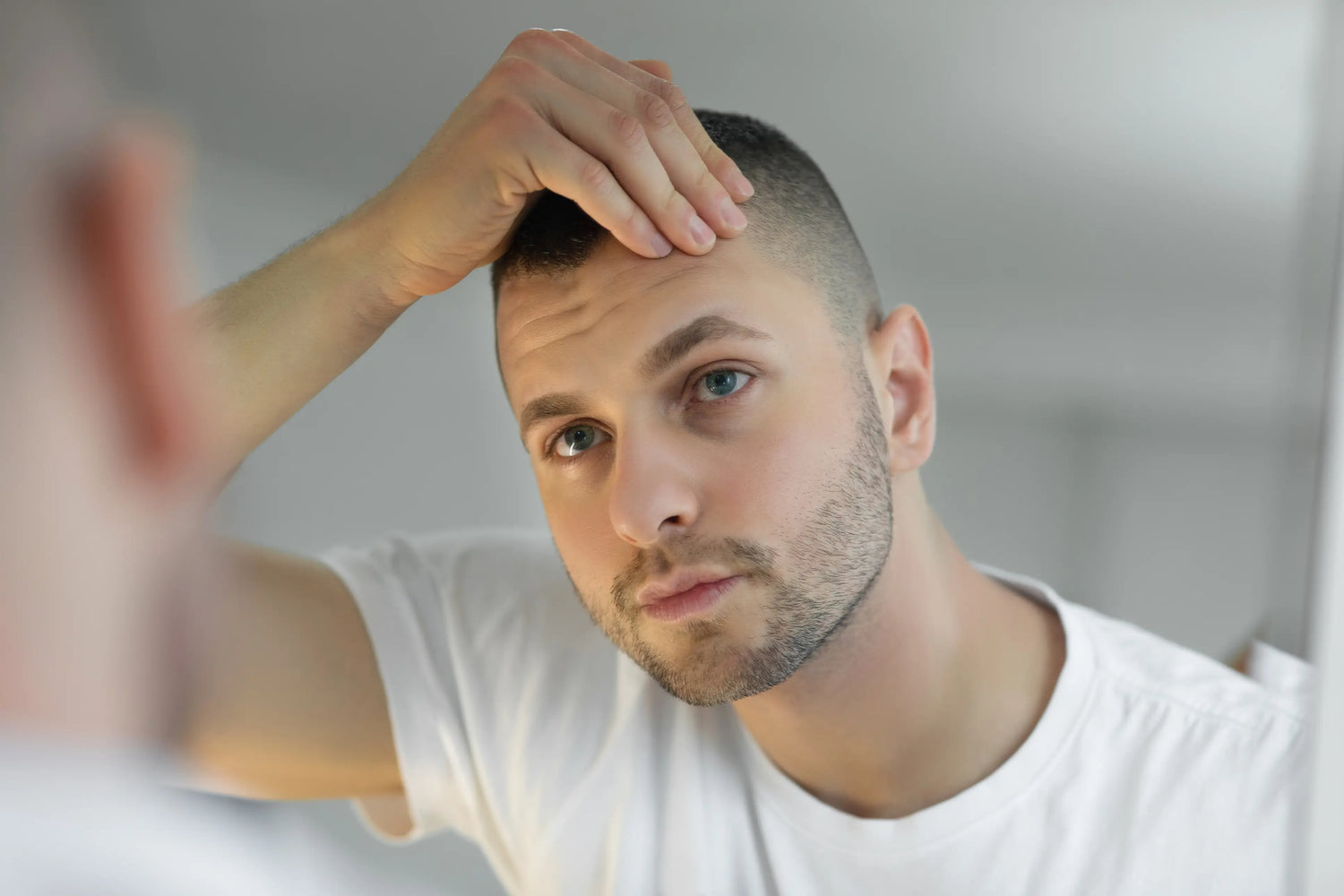 Hidrofobia capilar: o que é e como recuperar a saúde dos fios Homem em frente ao espelho arrumando o cabelo com a mão.