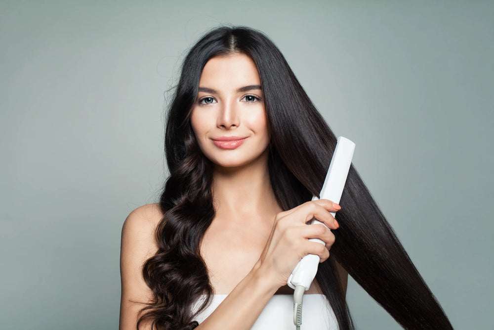 Como cuidar do cabelo com progressiva? Mulher com cabelo liso, usando uma chapinha para alisar os cabelos longos e saudáveis, apresentando um sorriso e um visual moderno.