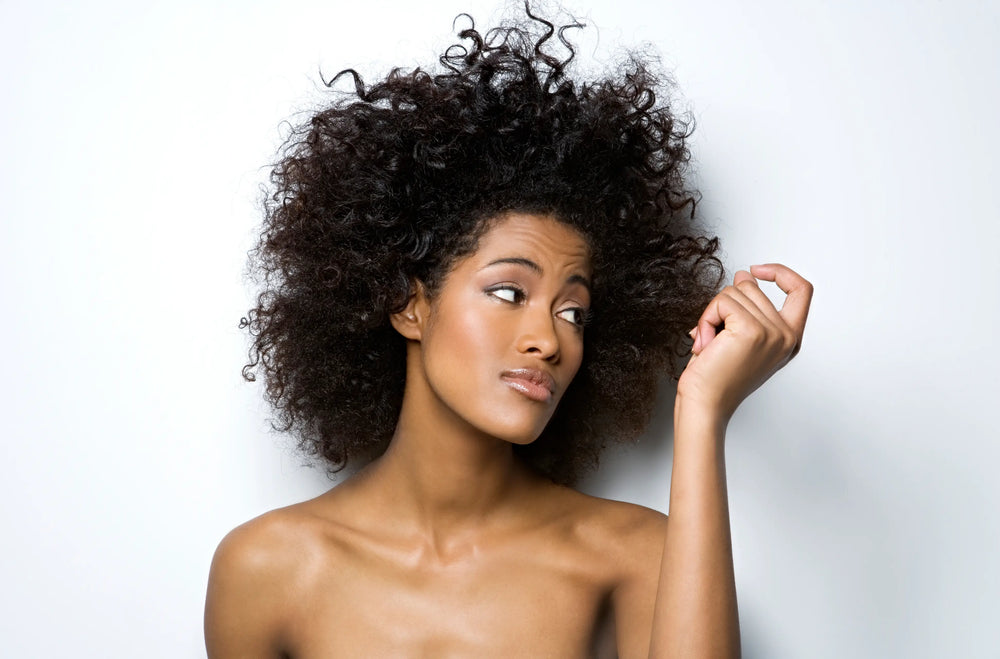 Como finalizar o cabelo em transição capilar Mulher com cabelo cacheado volumoso e expressão pensativa, destacando sua beleza natural em fundo neutro.