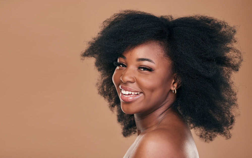 Cabelo virgem: quais os cuidados essenciais? Uma mulher sorridente com cabelo afro, destacando sua beleza natural e autoconfiança contra um fundo neutro, ideal para campanhas de autoestima.