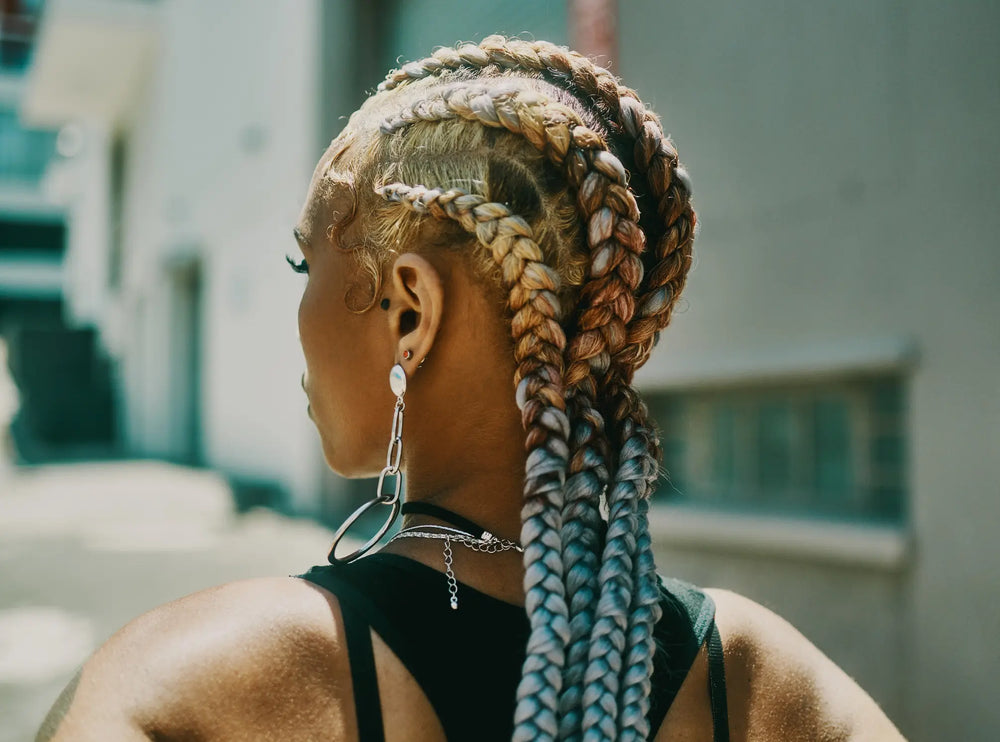 Crochet braids: conheça a técnica e os principais cuidados Imagem de mulher com tranças estilizadas e acessórios, destacando a beleza e a textura dos cabelos presos. A luz natural destaca as nuances e o penteado