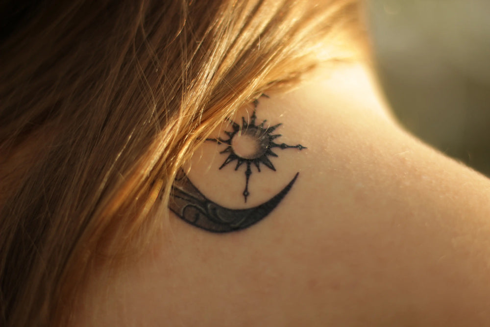 E aí, pode usar protetor solar na tatuagem mesmo? Tatuagem estilizada de sol e lua no ombro, destacando um design artístico.