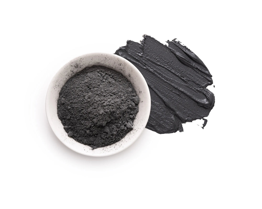 Pote com argila preta em pó e uma camada de argila em uma superfície branca.
