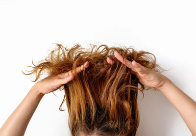 Mulher com cabelo cacheado levantando as mãos na cabeça, destacando a textura e o volume dos fios. Ideal para dicas de cuidados e estilo de cabelo.