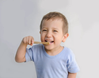 Criança sorridente escovando os dentes com uma escova de dente de bambu, promovendo a importância da higiene bucal infantil.