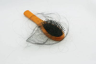 Escova de cabelo laranja com fios de cabelo emaranhados, ilustrando como prevenir queda de cabelo, cuidados capilares e manutenção de escovas.