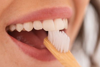 Pessoa escovando os dentes com escova de bambu mostrando sorriso saudável e dentes brancos. A escovação adequada é essencial para a higiene bucal.