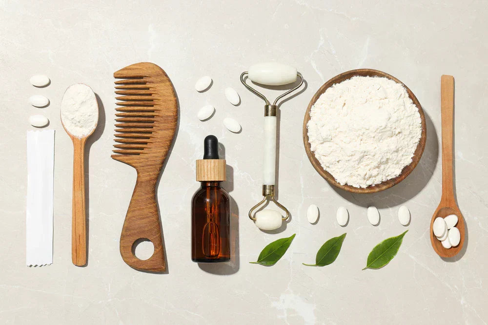 Arranjo de ferramentas de beleza, incluindo pente de madeira, frasco de óleo, colher, rolo facial e ingredientes em pó, ideal para cuidados com a pele.