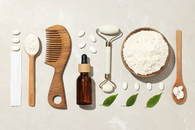 Arranjo de ferramentas de beleza, incluindo pente de madeira, frasco de óleo, colher, rolo facial e ingredientes em pó, ideal para cuidados com a pele.