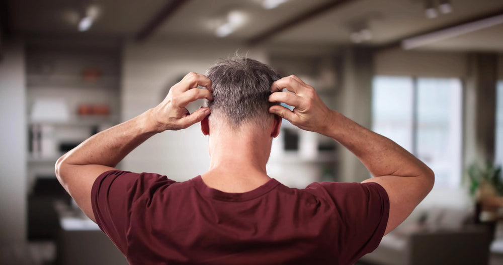 Homem com cabelo curto coçando a cabeça em um ambiente interno. A imagem retrata uma sensação de desconforto ou estresse.