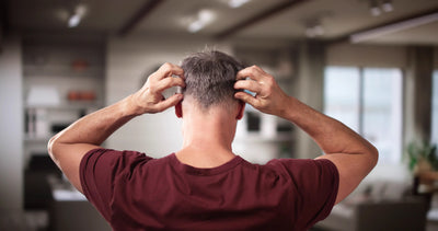 Homem com cabelo curto coçando a cabeça em um ambiente interno. A imagem retrata uma sensação de desconforto ou estresse.