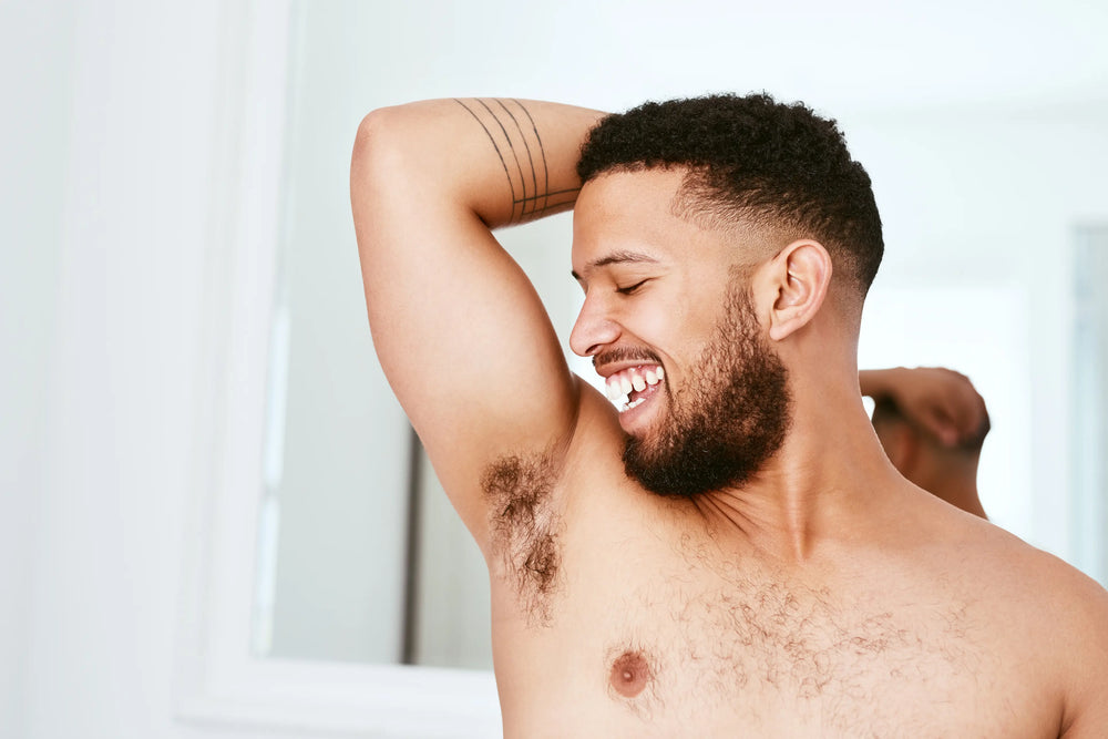 Homem sorridente exibindo axilas, com destaque para a autoestima e bem-estar, em ambiente claro e relaxado.