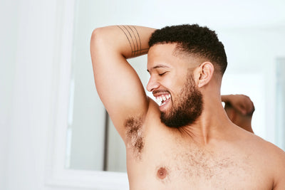 Homem sorridente exibindo axilas, com destaque para a autoestima e bem-estar, em ambiente claro e relaxado.