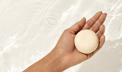 Imagem de uma mão segurando um shampoo em barra branco. 