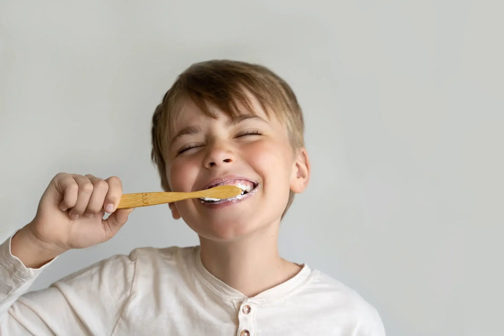 Criança sorridente escovando os dentes com uma escova de dente de madeira.