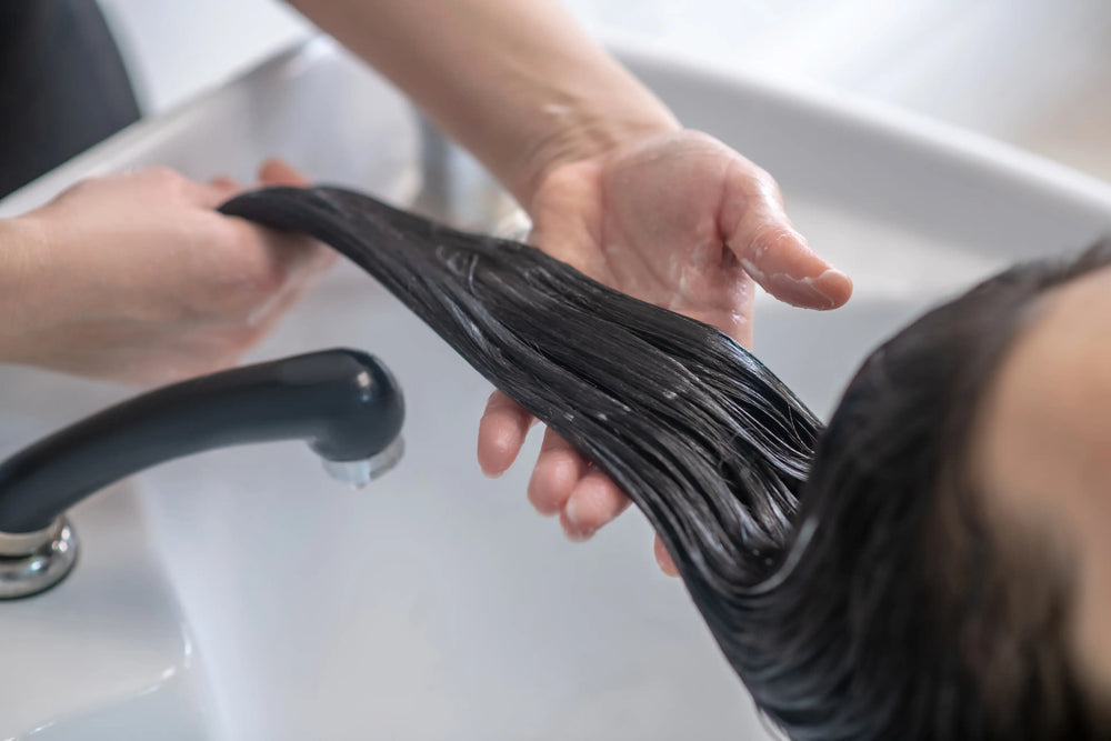 Cabeleireiro aplicando tratamento em cabelo longo e liso em um salão de beleza.