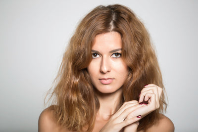 Modelo com cabelo cacheado e volumoso, expressando confiança em fundo neutro, destacando a beleza natural e os detalhes do rosto.