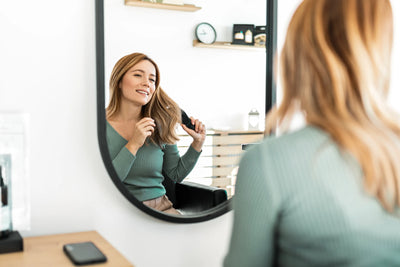 Mulher escovando cabelo saudável em frente ao espelho. 
