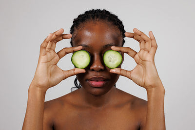 Mulher segurando fatias de pepino sobre os olhos, representando um momento relaxante de cuidados de beleza e autocuidado.