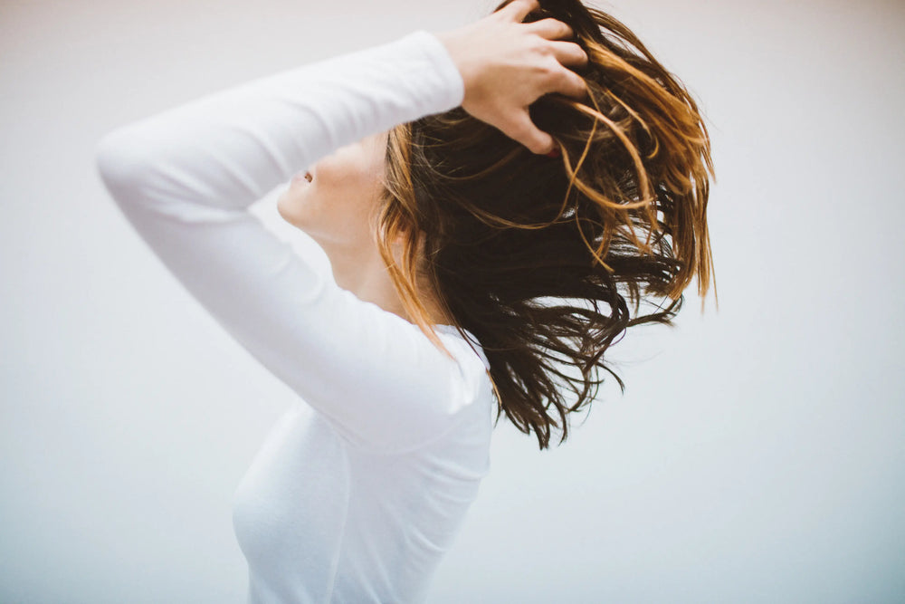 Mulher movimentando os cabelos em um fundo neutro, transmitindo leveza e liberdade com um ar de espontaneidade.
