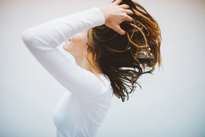 Mulher movimentando os cabelos em um fundo neutro, transmitindo leveza e liberdade com um ar de espontaneidade.