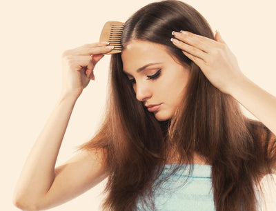 Mulher com cabelo longo penteando os fios com um pente de madeira, demonstrando cuidados com a beleza e a saúde capilar em um fundo claro.