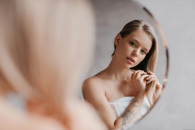 Mulher loira se olhando no espelho com cabelo solto, com a luz suave iluminando o ambiente.