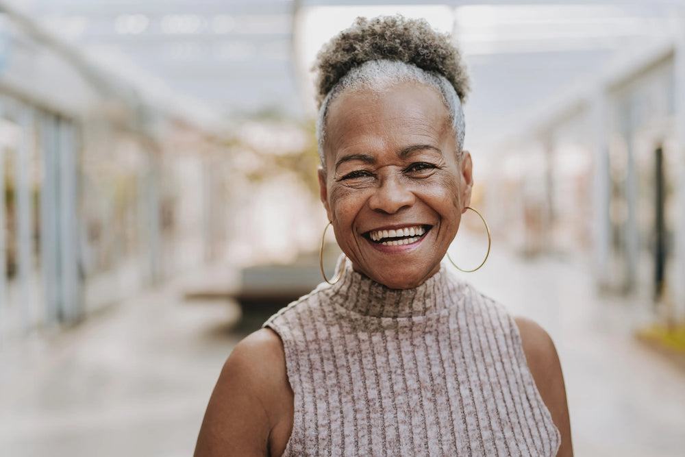 Mulher sorridente com cabelo crespo e olhar amigável em um ambiente moderno, celebrando a beleza e a alegria da vida. Ideal para temas de autoestima e bem-estar.