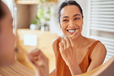 Mulher sorridente escovando os dentes em frente ao espelho, promovendo cuidados dentários e saúde bucal. Rotina de higiene pessoal.