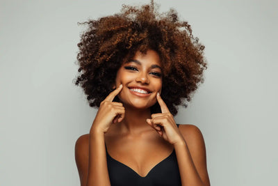 Mulher sorridente com cabelo volumoso, mostrando simpatia, em um fundo neutro.