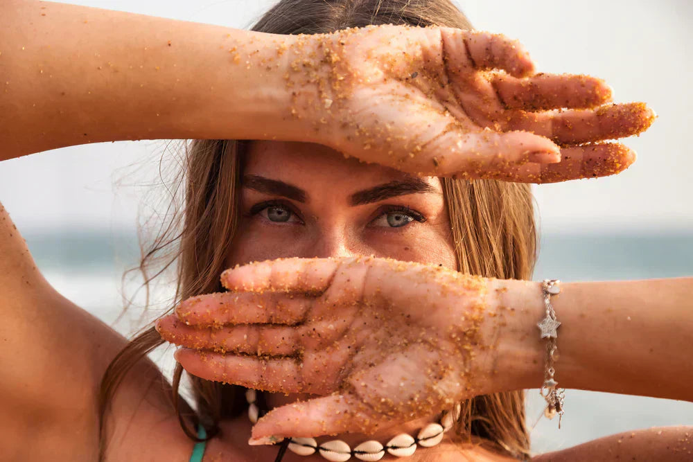 mulher loira de olhos claros na praia com as mãos sujas de areia