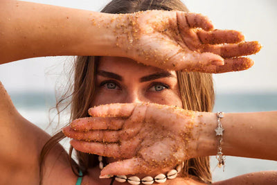 mulher loira de olhos claros na praia com as mãos sujas de areia