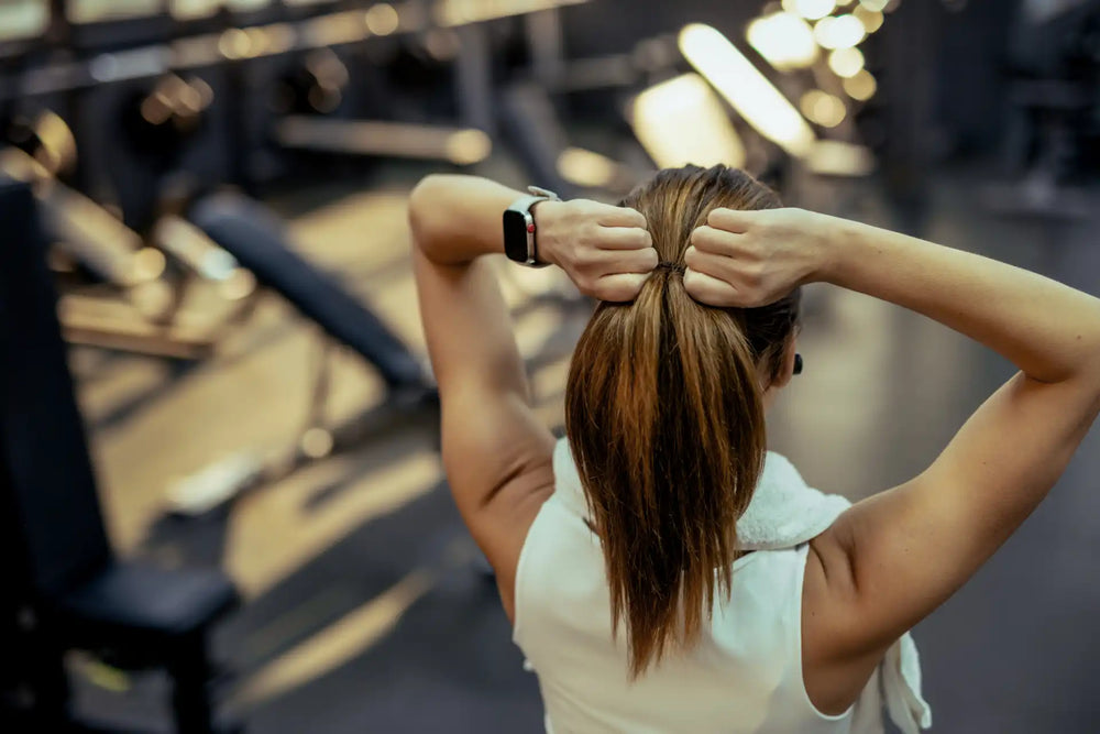 Mulher preparando-se para malhar em uma academia, ajustando o cabelo para o treino.