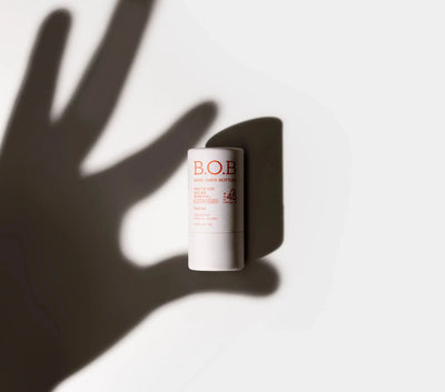Produto B.O.B. com proteção solar para a pele, destacado com sombra de uma mão sobre fundo claro, ideal para cuidados faciais com FPS 45.