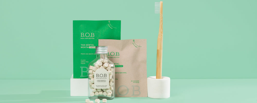 Produtos B.O.B de higiene bucal com pasta dental natural, frasco com pastilhas e escova de dente sustentável em fundo verde.