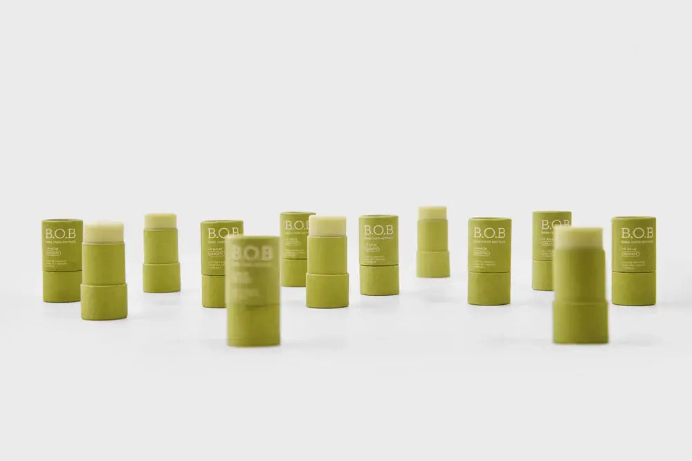 Vários produtos lip balm na embalagem verde da marca B.O.B, sobre um fundo neutro.