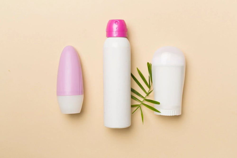 Imagem de três tipos de desodorantes: spray, roll-on e creme, com uma folha ao lado, em fundo neutro.